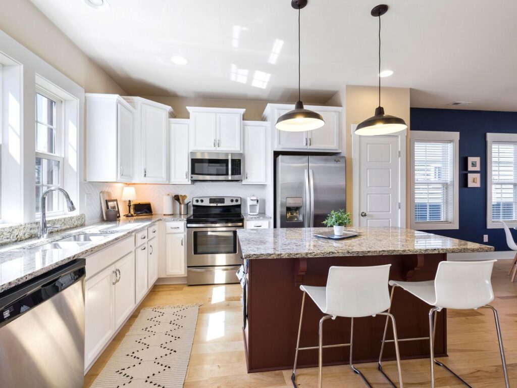 Modern kitchen with white cabinets, stainless steel appliances, and a central island with two white chairs, maintained to perfection with regular monthly cleaning.